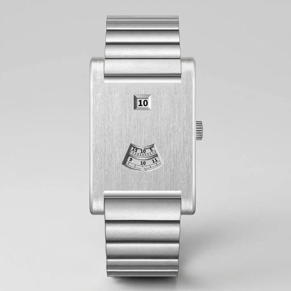 A minimalist silver stainless steel wristwatch with a rectangular bezel, a fluted metal link bracelet, a small digital day display, and a small analog hour indicator on the dial, shown against a neutral light gray background.