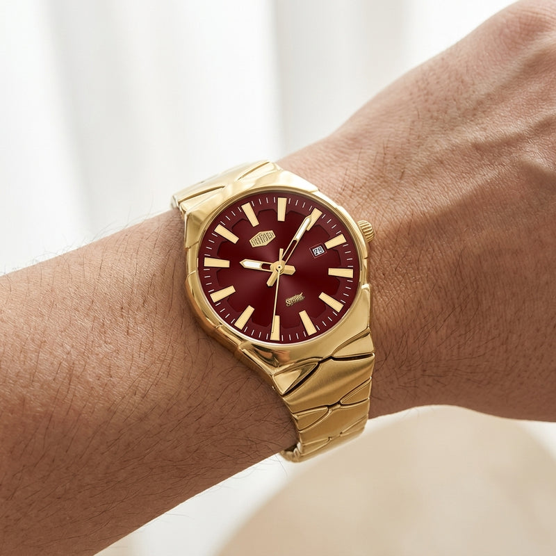 A gold-tone wristwatch with a deep burgundy dial, shown worn on a person's wrist against a soft, light background.