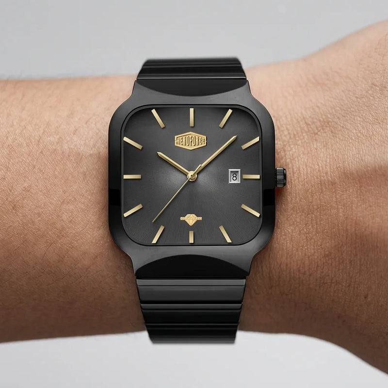 A black rectangular analog watch with gold-tone hands, hour markers, and logo details, shown worn on a person's wrist against a light gray background.