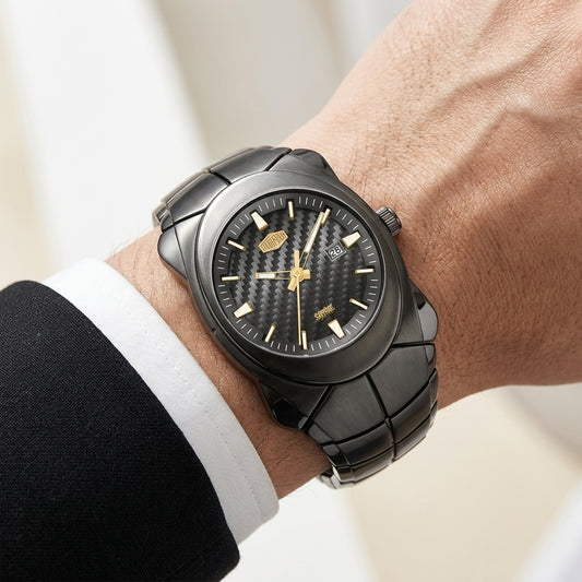 A close-up lifestyle shot of a man's wrist wearing a black ceramic watch with gold-tone hands and markers. The watch is shown on a person's wrist with a white dress shirt cuff and dark suit jacket visible, set against a softly blurred indoor background.