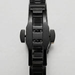 A close-up of a black metal watch band and case, showing the side crown screws and brushed and polished links, on a light gray background.