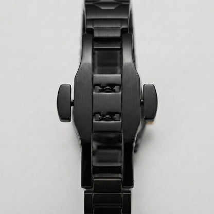 A close-up of a black metal watch band and case, showing the side crown screws and brushed and polished links, on a light gray background.
