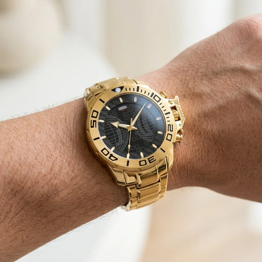 A gold-tone stainless steel watch with a black dial and bezel, worn on a person's wrist against a soft, out-of-focus light background.