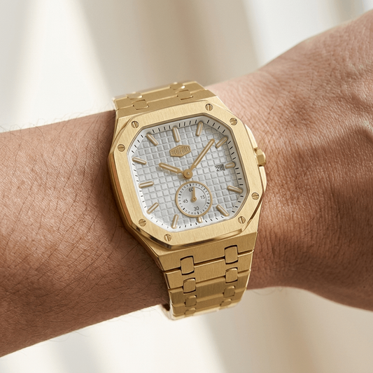 A gold-tone stainless steel watch with a textured Silver white dial and matching gold link bracelet, shown worn on a person's wrist against a soft beige background.