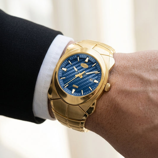 A gold-tone watch with a textured blue dial and matching blue links bracelet, worn on a man's wrist dressed in a black suit jacket and white dress shirt.