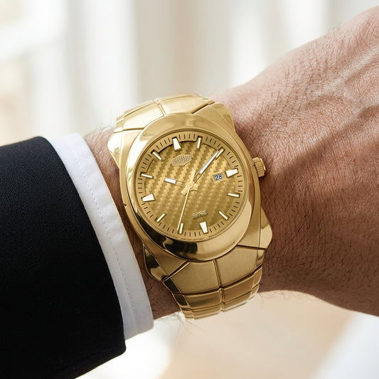 A gold-tone watch with a textured dial and integrated bracelet worn on a person's wrist, shown against a softly blurred light background. The person is dressed in a black suit jacket and white dress shirt.