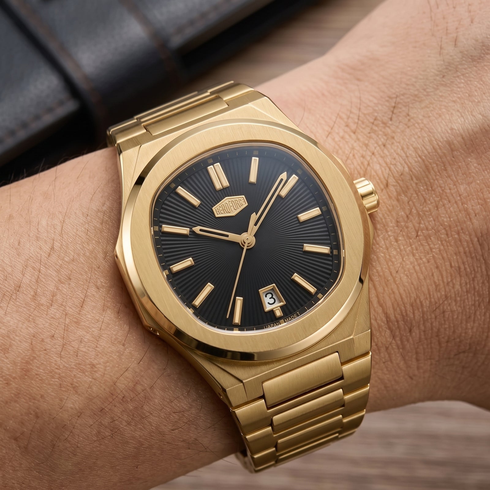 A gold-tone wristwatch with a black sunburst dial and matching gold-tone metal bracelet, shown worn on a person's wrist.