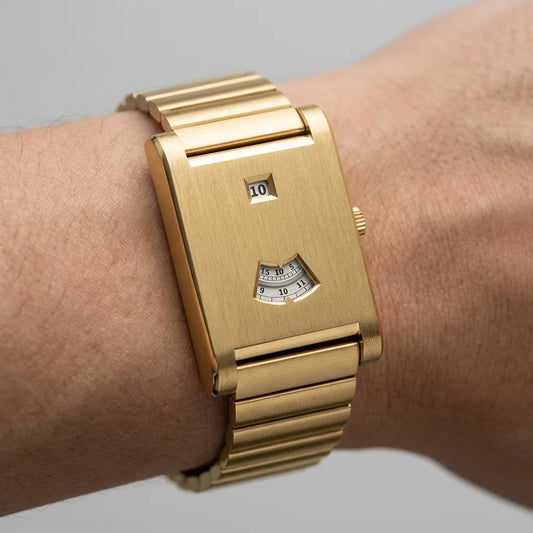 A gold-tone wristwatch with a rectangular case and matching metal link bracelet, shown worn on a person's wrist against a light gray background.