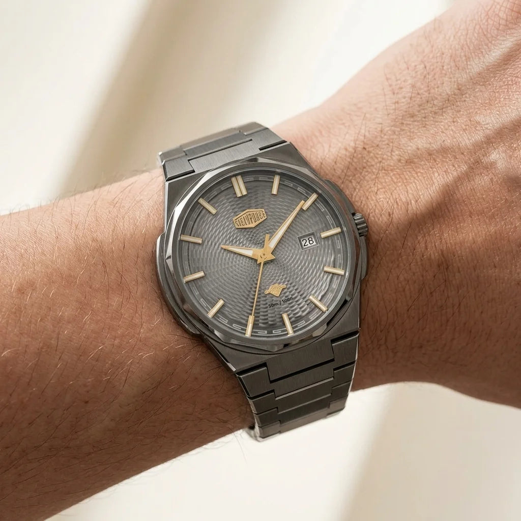 A men's stainless steel watch with a textured gray dial and gold-tone hands, shown worn on a person's wrist against a soft beige background.