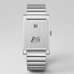A minimalist silver stainless steel wristwatch with a rectangular bezel, a fluted metal link bracelet, a small digital day display, and a small analog hour indicator on the dial, shown against a neutral light gray background.