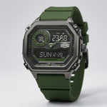 A rugged digital watch with an olive green silicone strap, a dark gray metallic case, and a black face with green accents, shown on a light gray background.