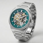 A silver-tone stainless steel skeleton wristwatch with a teal blue dial, showcasing the intricate gold and silver mechanical movement through an open case.