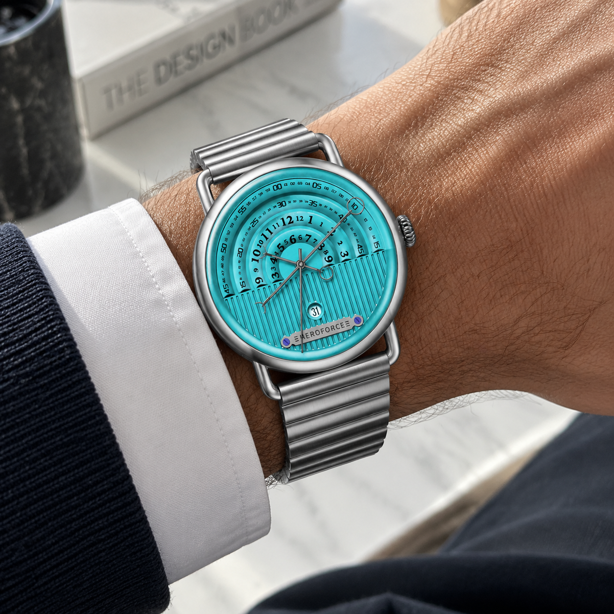 A silver-toned metal wristwatch with a bright turquoise dial and matching metal link bracelet, worn on a person's wrist over a white dress shirt cuff.