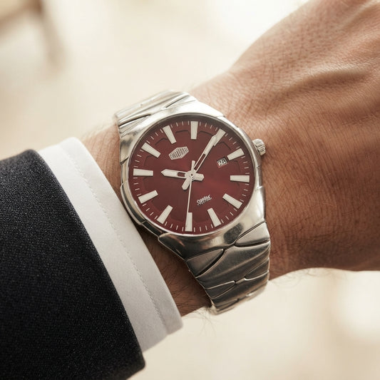 A silver metal wristwatch with a deep burgundy dial and silver link bracelet, shown worn on a person's wrist with a white dress shirt cuff and dark suit jacket visible.