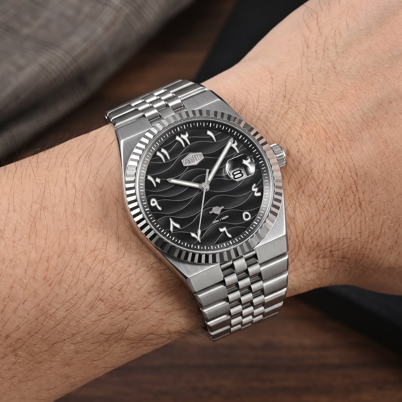 A silver stainless steel wristwatch with a black dial and wave-pattern subdials, shown worn on a person's wrist.