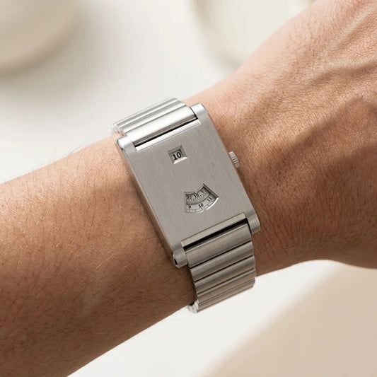 A silver stainless steel wristwatch with a rectangular case and integrated metal link bracelet, shown worn on a person's wrist.