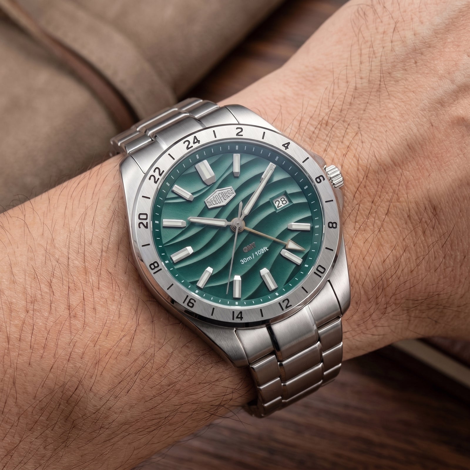 A stainless steel wristwatch with a green wave-pattern dial and silver-tone metal bracelet, shown worn on a person's wrist.