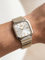 A two-tone wristwatch with a silver and gold-tone metal bracelet and a white dial, shown worn on a person's wrist.