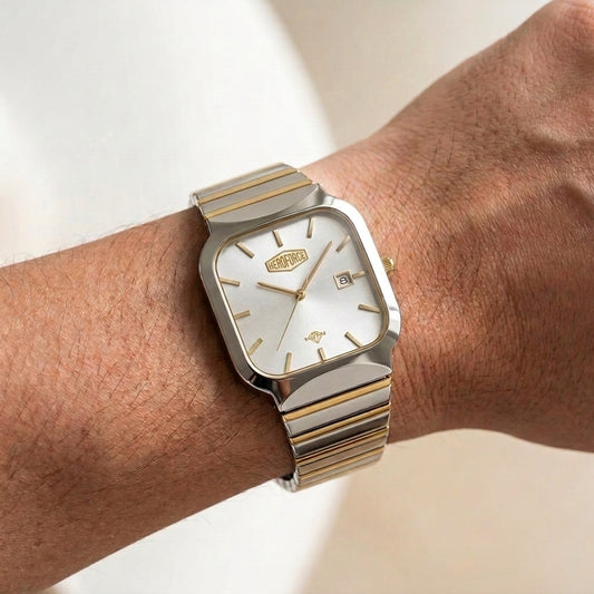 A silver and gold-tone wristwatch with a white dial, shown worn on a person's wrist against a light beige background.
