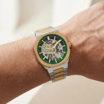 A wristwatch with a green dial and gold-and-silver two-tone metal bracelet, shown worn on a hand