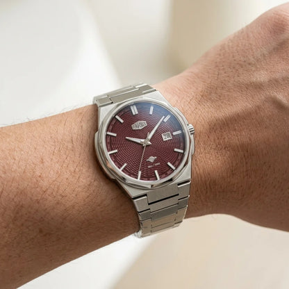 A wristwatch with a silver stainless steel bracelet and case, featuring a textured dark red dial, shown worn on a person's wrist.