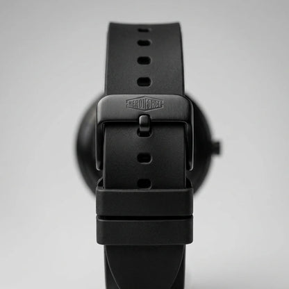 Close-up of a black watch strap buckle with the brand name debossed on the metal clasp, set against a soft gray background.