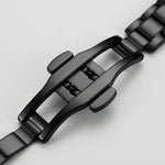Close-up of a black metal watch band clasp and links on a light gray background.