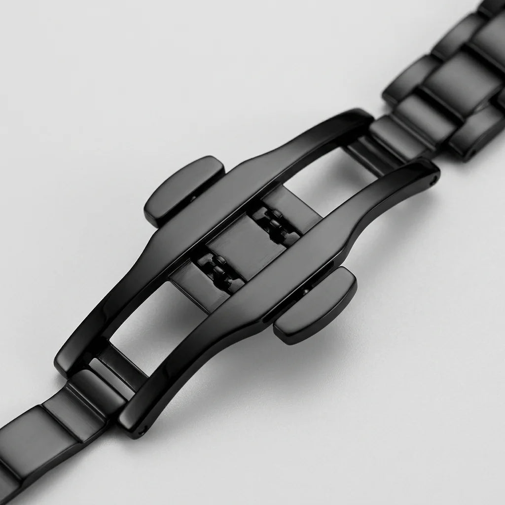 Close-up of a black metal watch band clasp and links on a light gray background.