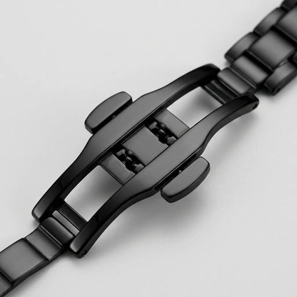 Close-up of a black metal watch band clasp and links on a light gray background.