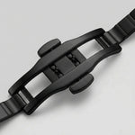 Close-up of a black metal watch strap buckle and adjacent links on a light gray background.