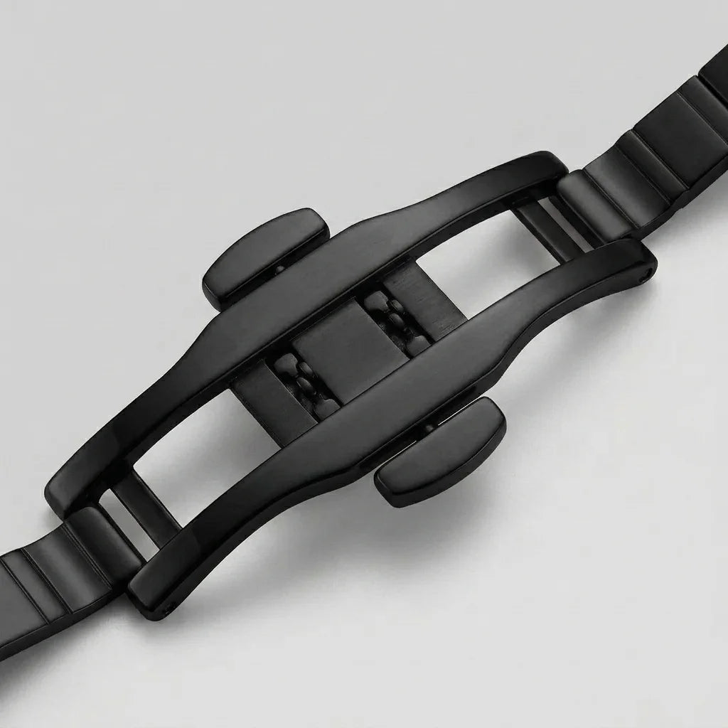 Close-up of a black metal watch strap buckle and adjacent links on a light gray background.