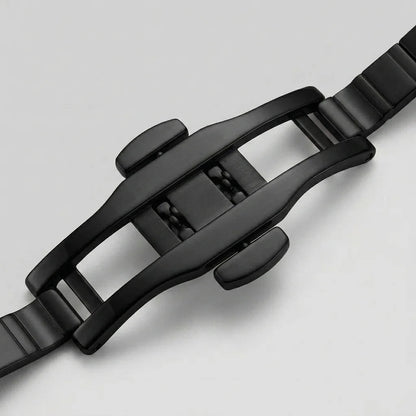 Close-up of a black metal watch strap buckle and adjacent links on a light gray background.