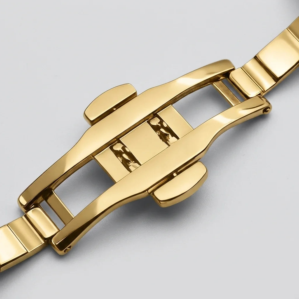 Close-up of a polished gold-tone metal watch band clasp on a light gray background.