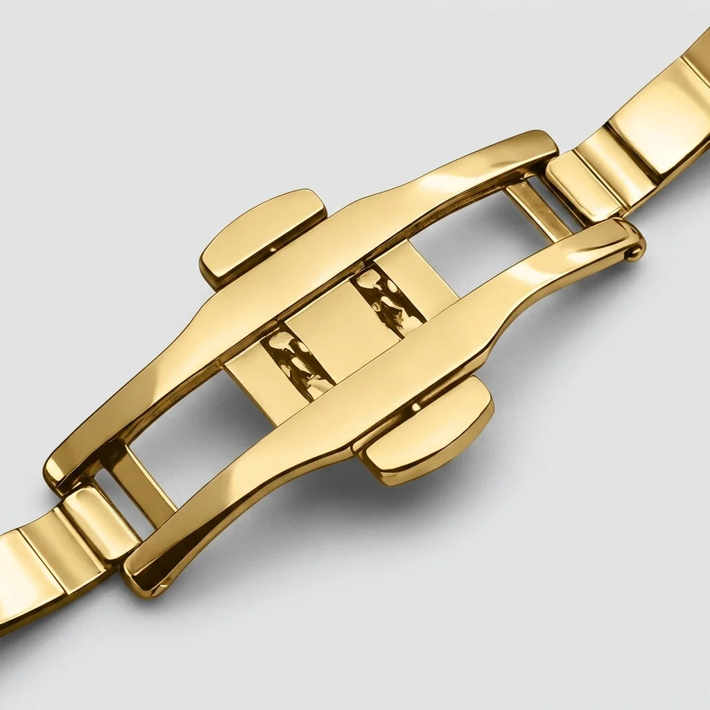 Close-up of a polished yellow gold stainless steel watch clasp and bracelet links on a light gray background.