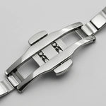 Close-up of a polished stainless steel watch band clasp on a light gray background.