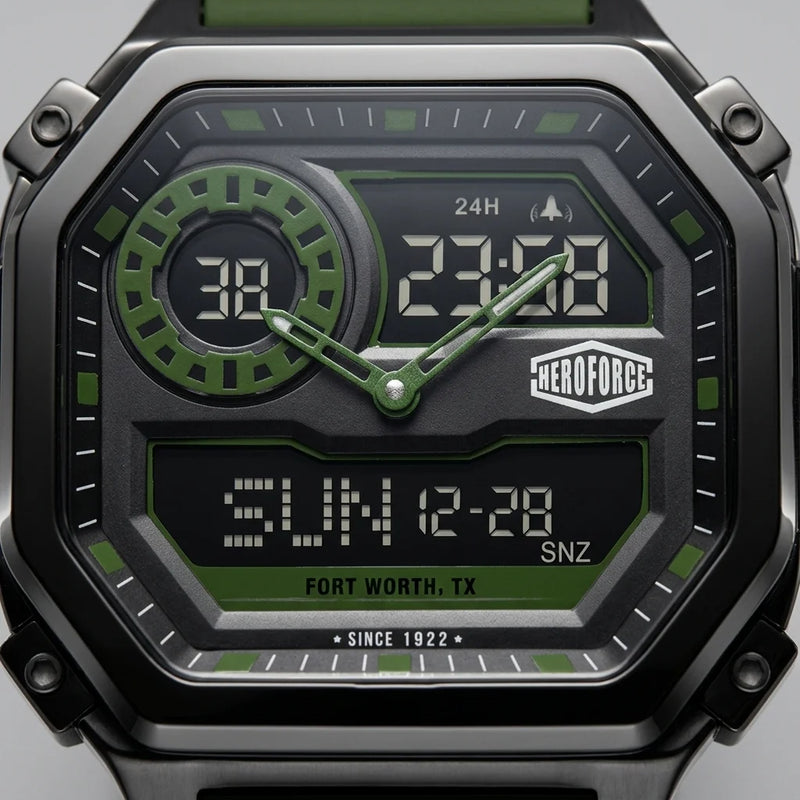 Close-up of a rugged digital watch with a black and dark gray case, green accents, and a black dial displaying time and date details. The brand name HEROFORCE is visible on the watch face.