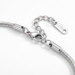 Close-up of a silver-toned snake chain bracelet showing the lobster clasp, extension chain, and a polished tag engraved with 'SS STEEL' .
