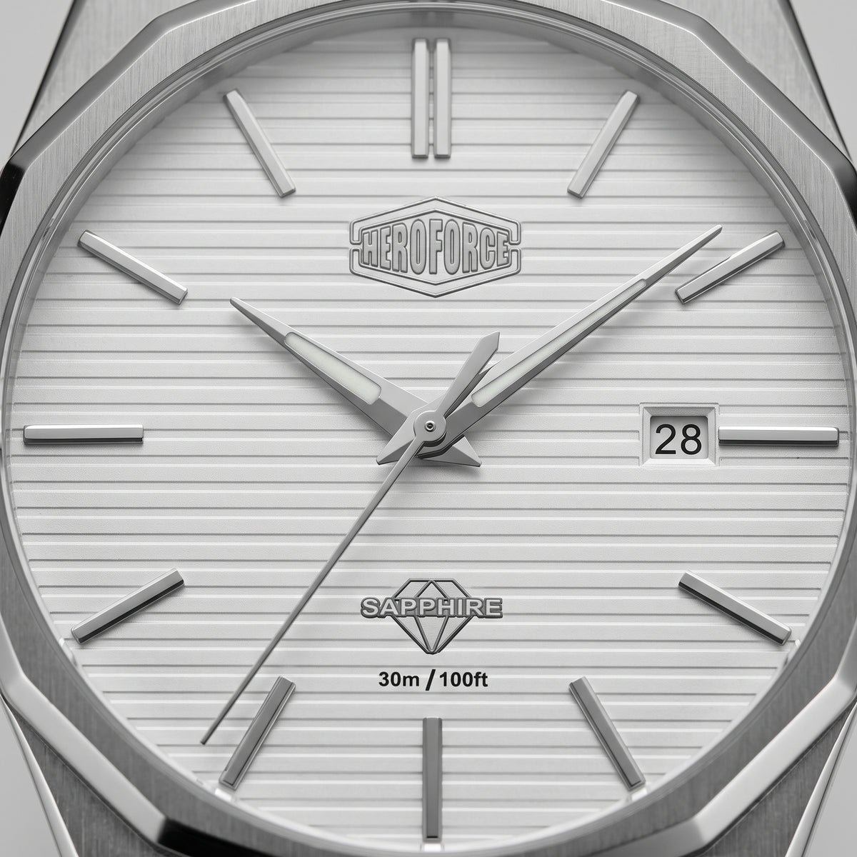 Close-up of a silver-toned watch dial with a white textured face, angular metal hour markers, silver hands, a date window showing 28, and the Heroforce logo at the top center.