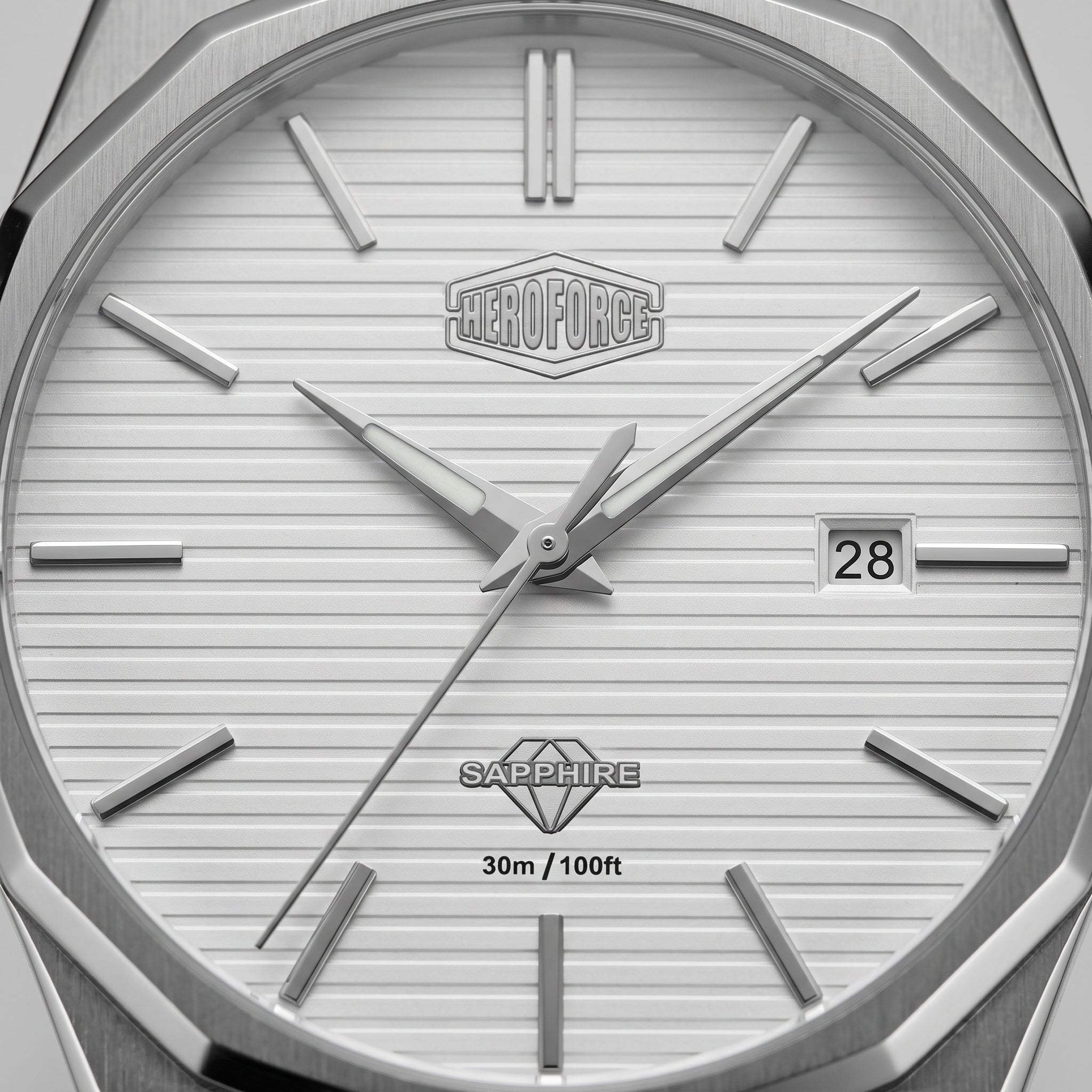 Close-up of a silver-toned watch dial with a white textured face, angular metal hour markers, silver hands, a date window showing 28, and the Heroforce logo at the top center.