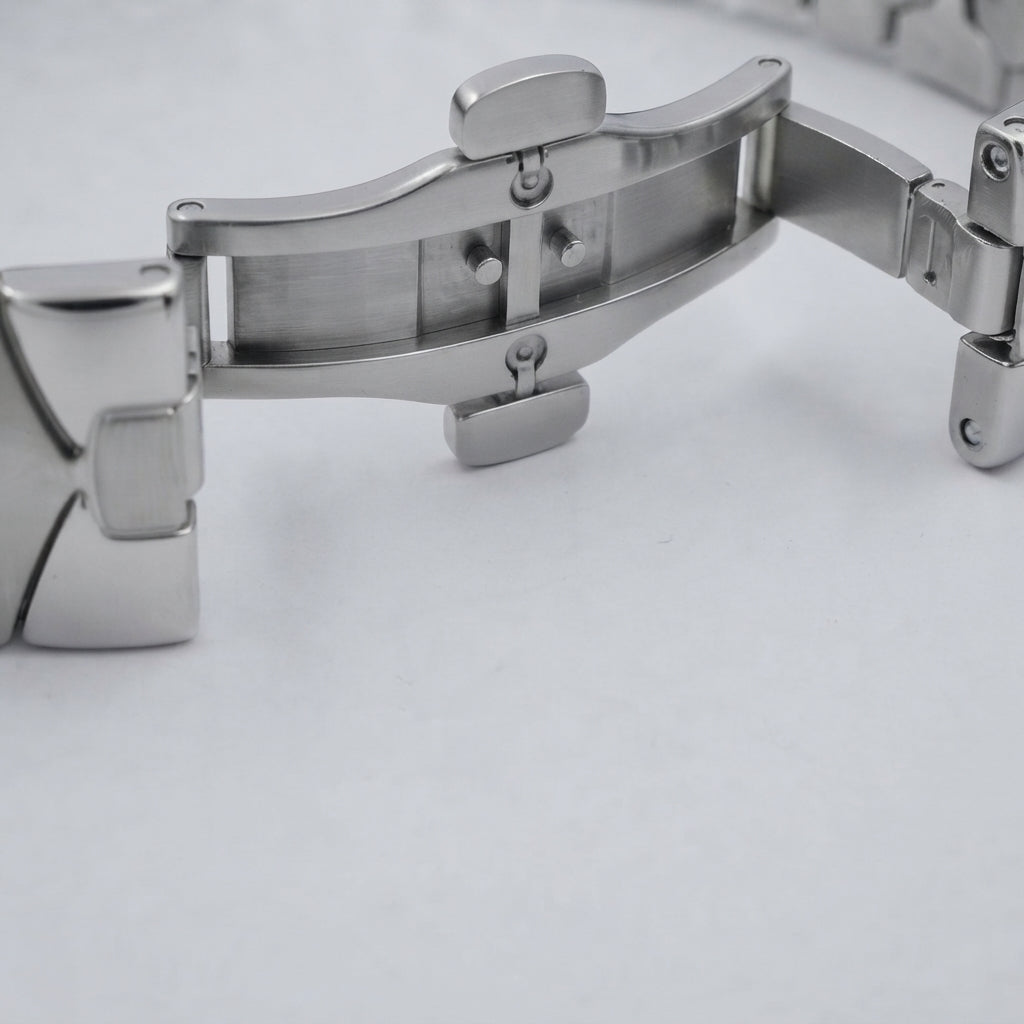 Close-up of a stainless steel watch band clasp on a light gray background.