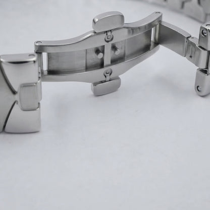 Close-up of a stainless steel watch band clasp on a light gray background.