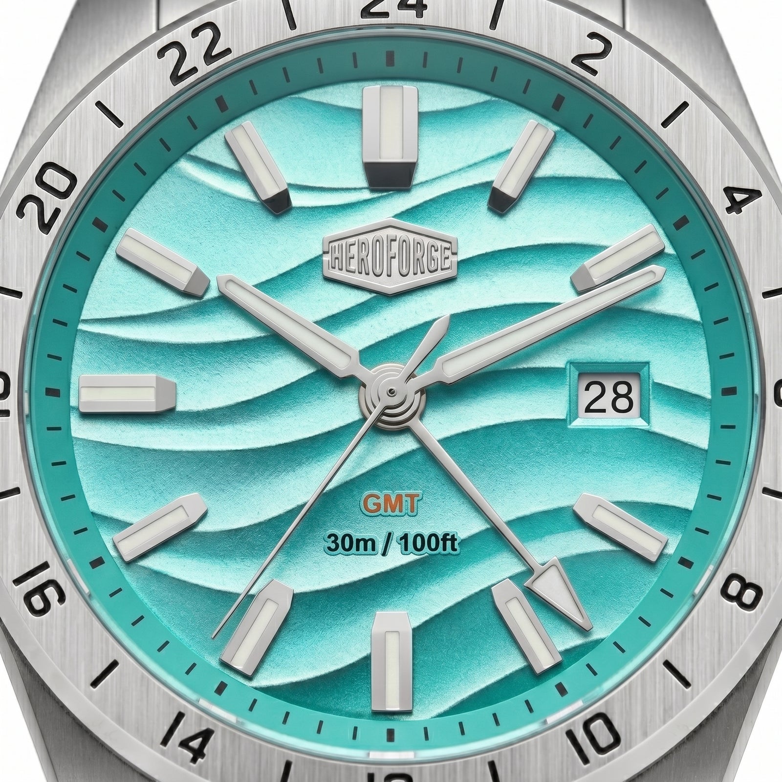 Close-up of a wristwatch dial and bezel. The watch has a brushed silver-tone metal case and bezel, a turquoise and aqua wavy patterned dial.