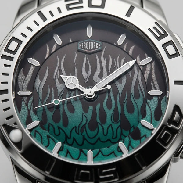 Close-up of a wristwatch dial and bezel with a silver stainless steel case, black outer ring, and a dark dial featuring a teal-to-black flame pattern. The brand name HEROFORCE is visible above the 12 o'clock mark.