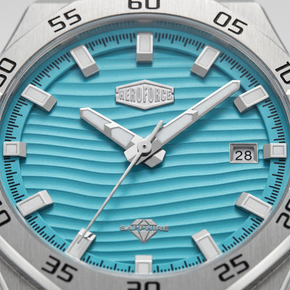 Close-up of a wristwatch dial with a bright turquoise blue wavy textured face, silver-tone hour markers and hands, a date window showing 28, and a stainless steel bezel with black minute markings.
