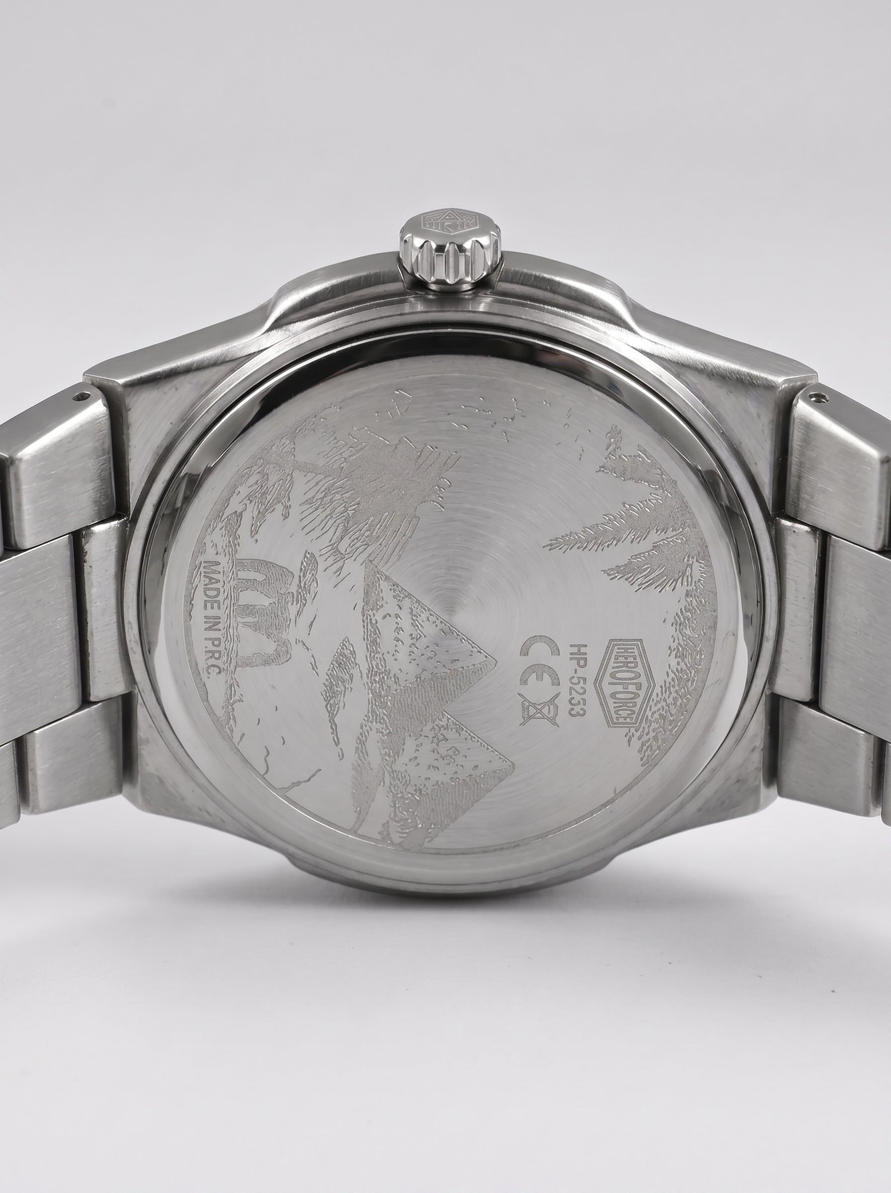 Close-up rear view of a stainless steel wristwatch with a metal link bracelet, showing the brushed case back engraved with a mountain design