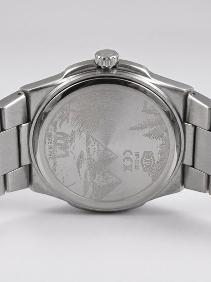 Close-up rear view of a stainless steel wristwatch with a metal link bracelet, showing the brushed case back engraved with a mountain design
