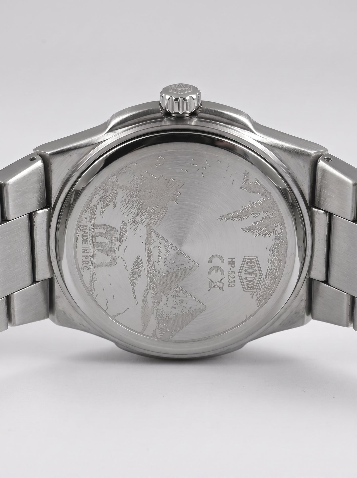 Close-up rear view of a stainless steel wristwatch with a metal link bracelet, showing the brushed case back engraved with a mountain design