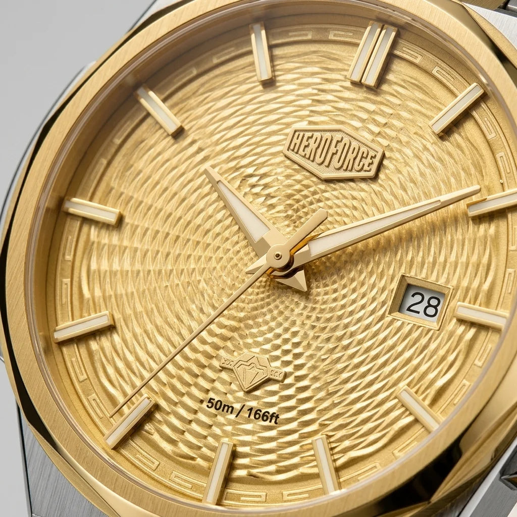 Gold-tone stainless steel watch dial close-up with a textured sunburst pattern, rectangular hour markers, gold hands, a date window showing 28, and the HEROFORCE logo above the 12 o'clock position.