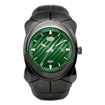 A rugged black watch with a glossy black resin case and integrated black strap, featuring a textured green carbon-fiber-style dial with silver-tone hands, baton markers, and a date window.