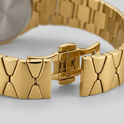 Close-up of a gold-tone metal watch band with a geometric link design and a folding clasp.